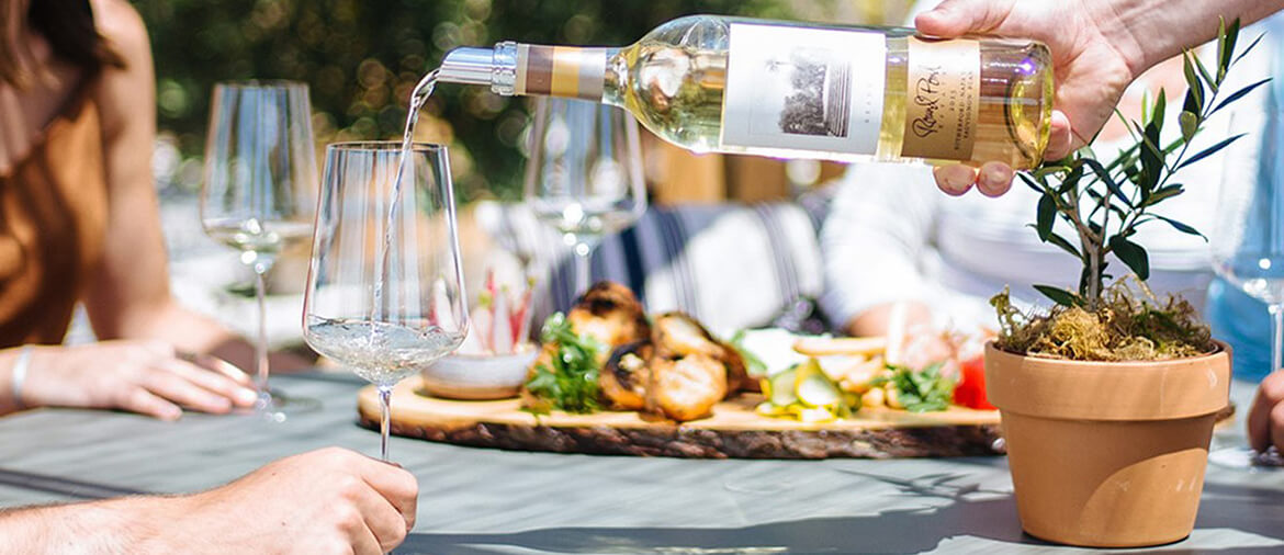 pouring a bottle of white wine at the table outdoors